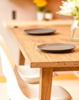 Antique Wooden dining table with two dark plates and a vase of flowers in a softly lit room.