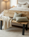 Wooden bench with pillows and a blanket in front of a bed in a bedroom setting.