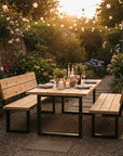 Outdoor dining setup with wooden table and benches in a garden at sunset.