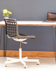 A desk top made from reclaimed scaffold boards, paired with a white office chair and decorative items. The desk is against a dark blue wall, on a wooden floor.