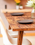 Flamed Wooden dining table with two black plates and white chairs in a softly blurred background