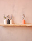 A rustic wooden shelf with floating brackets mounted on a wall, made from reclaimed scaffolding board displaying three vases containing flowers.