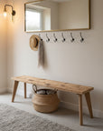 Wooden bench in a hallway with coat hooks and a basket underneath