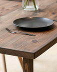 Jacobean Oak colour dining table with Black plate on a wooden table with a fork and a vase in the background