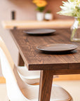 Wooden dining table with two plates and a vase of flowers in a softly blurred room setting. Jacobean Oak finish