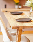 Natural Wooden dining table with two black plates and white chairs in a room.
