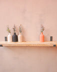 A reclaimed rustic wooden shelf with hanging brackets, displaying vases containing flowers.