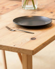 Wooden dining table with black plates and a fork on a light wooden floor.