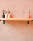 A reclaimed rustic wooden shelf mounted on a wall, using propped metal brackets, showcasing three vases.