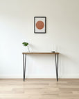 Wooden table with black legs against a white wall with a framed picture.