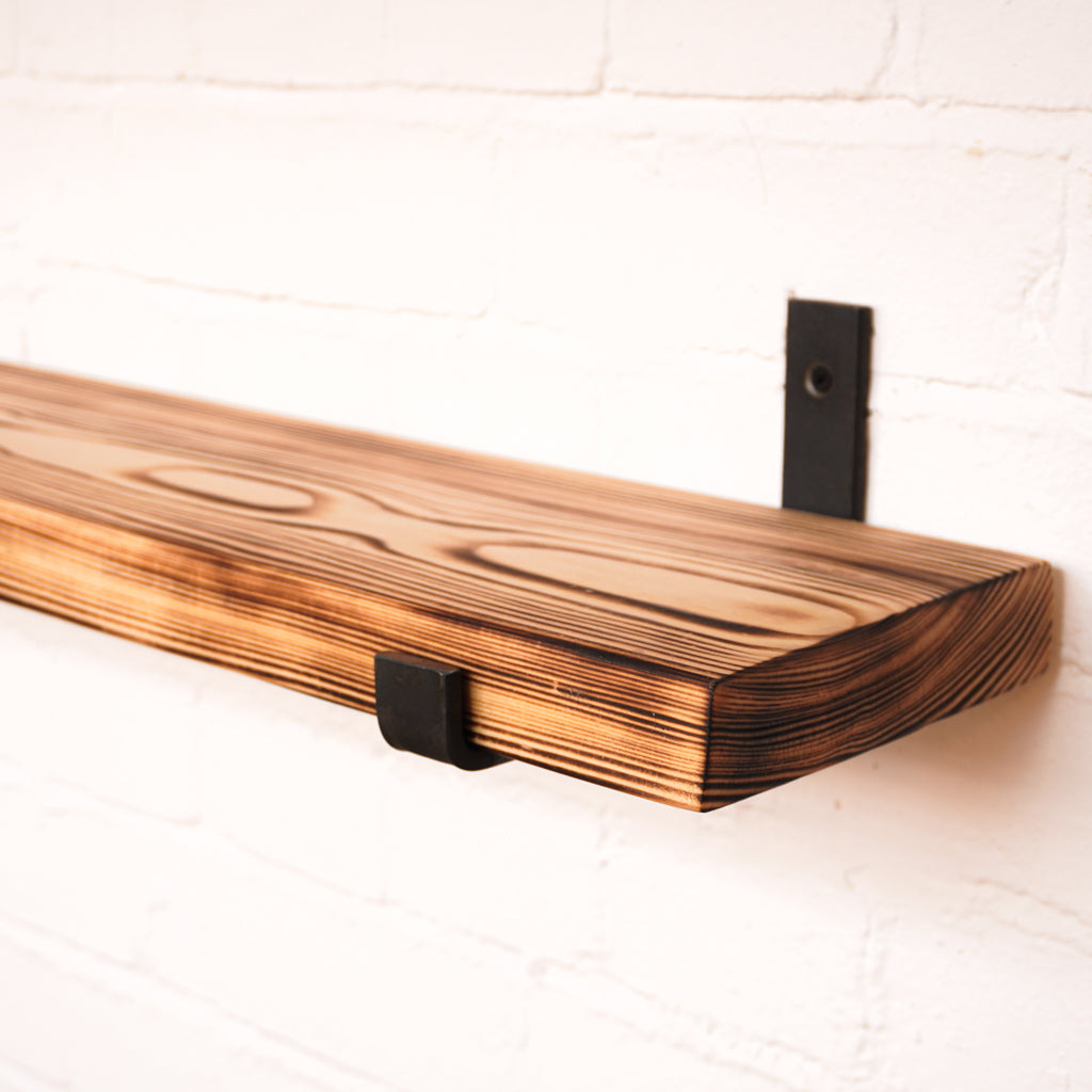Flamed wooden radiator shelf made from scaffolding boards with hanging brackets. 