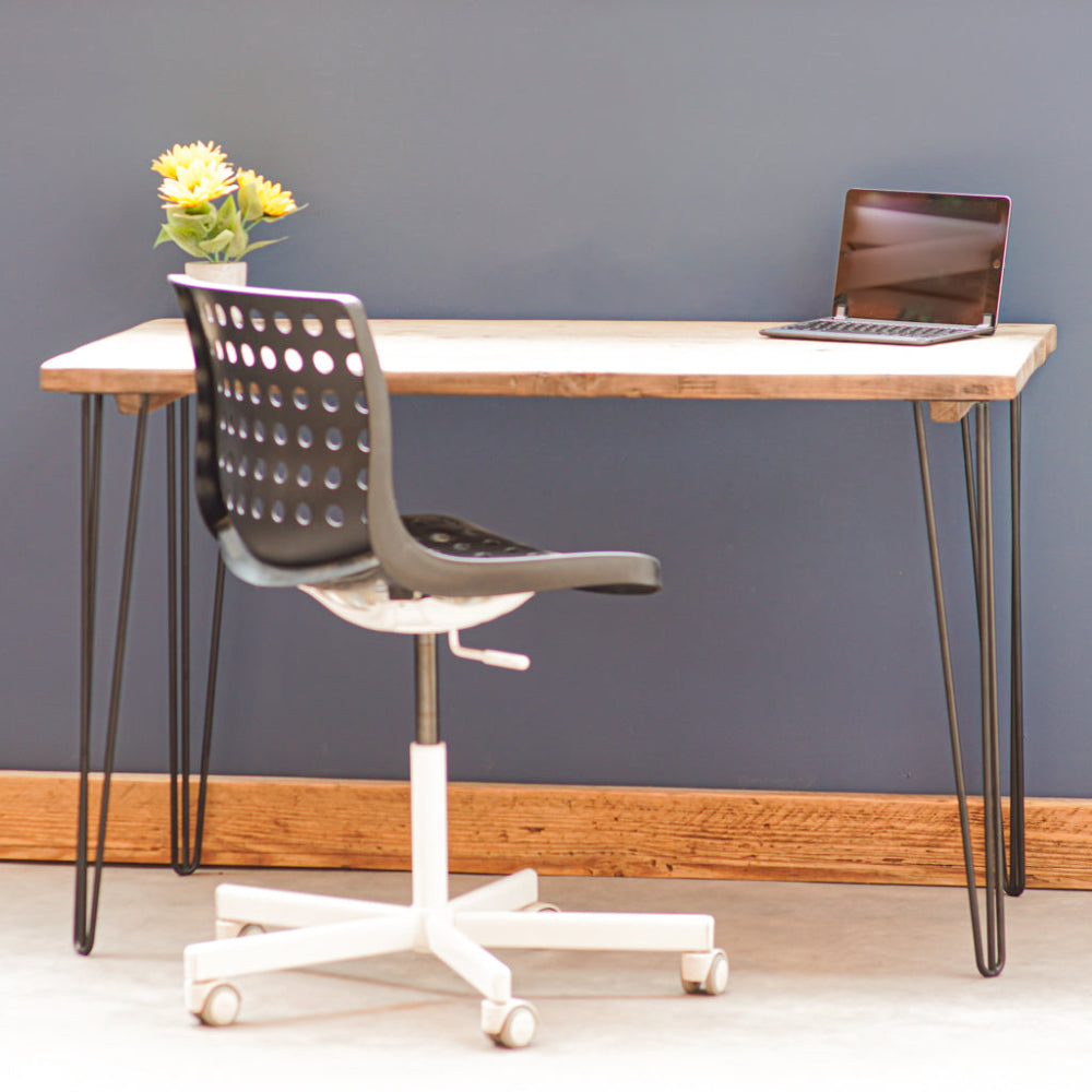 A desk top made from reclaimed scaffold boards, paired with a white office chair and decorative items. The desk is against a dark blue wall, on a wooden floor.