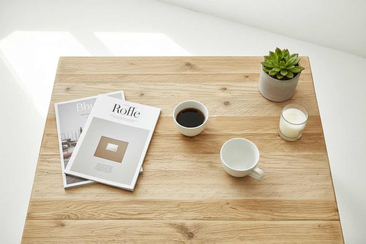 Wooden coffee table with magazines, coffee, and a plant on a white background