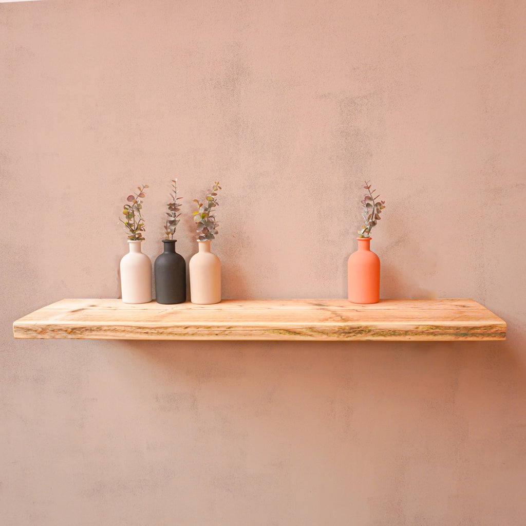 A reclaimed wooden floating shelf mounted on a wall, holding three vases with flowers.