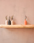 A reclaimed wooden floating shelf mounted on a wall, holding three vases with flowers.