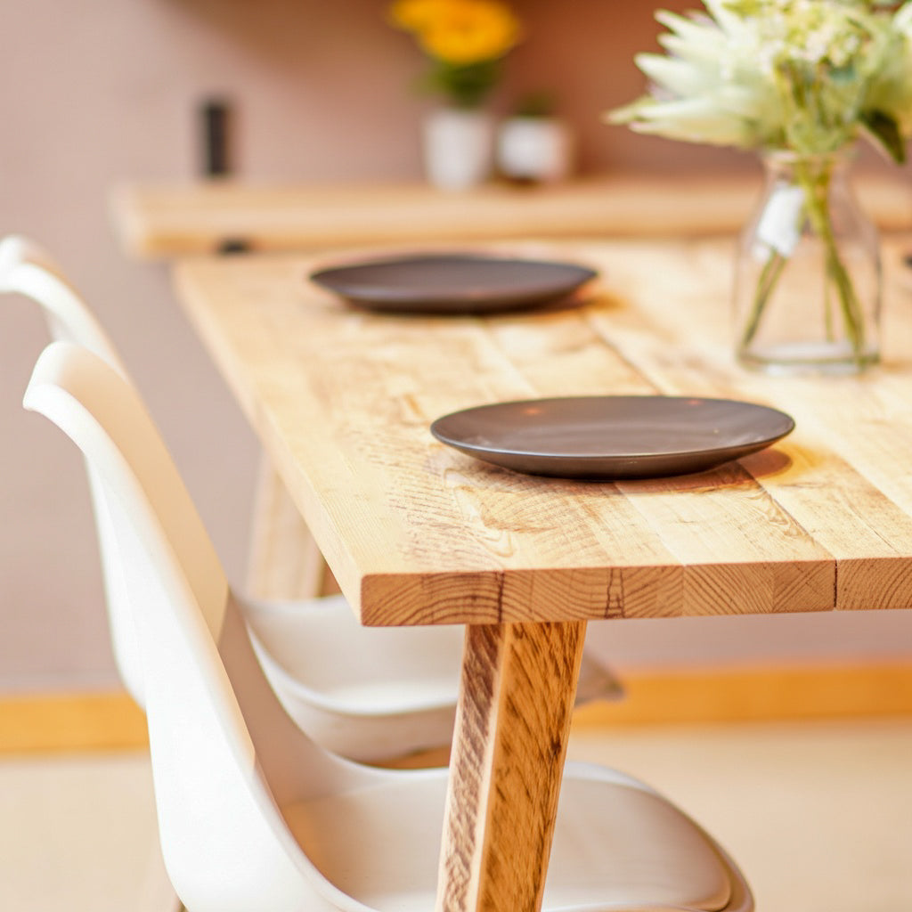 Natural Wooden dining table with two black plates and white chairs in a room.
