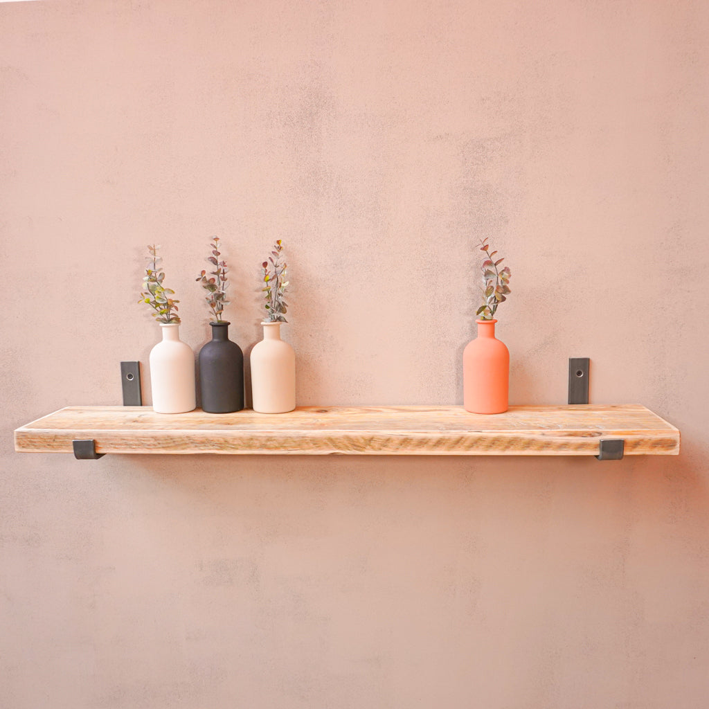 A reclaimed rustic wooden shelf with hanging brackets, displaying vases containing flowers.