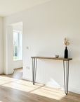 Console table with a vase and bowl in a bright room with large windows.
